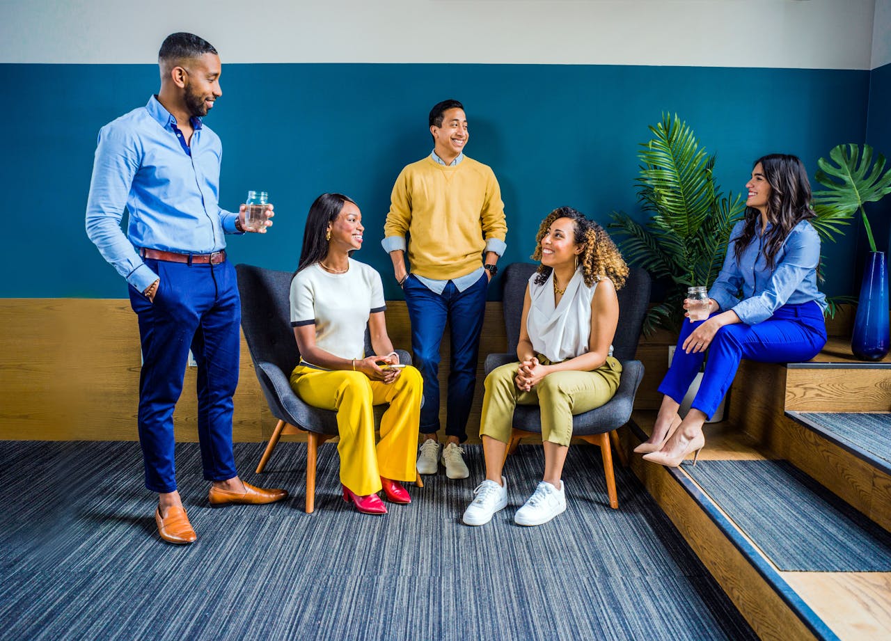 about-01 A diverse group of five professionals engaging in a casual indoor meeting, smiling and talking.